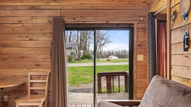 A wooden cabin interior with a sliding glass door leading to a deck, a sofa, and a wooden table.