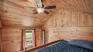 A wooden cabin room with a bed, a ceiling fan, and a window.