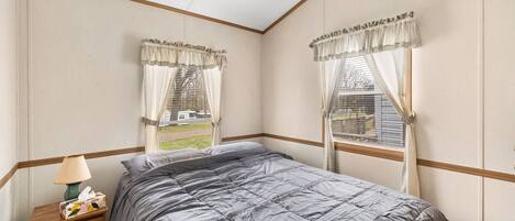 A bedroom with a bed, a nightstand, a lamp, and two windows with curtains.