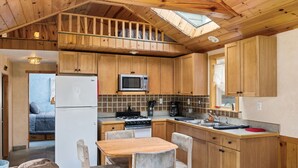 A compact kitchen with wooden cabinets, a microwave, a stove, and a refrigerator. There is a dining area with a table and chairs. - Vacation Home Rental PM 51 (Russell)