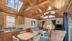A cozy cabin interior with wooden beams, a dining area, a sofa, and a TV. - Vacation Home Rental PM 51 (Russell)