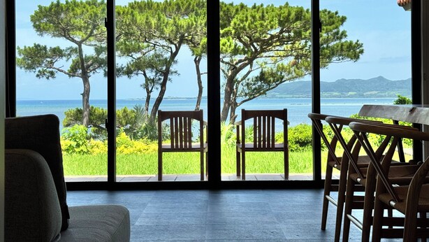 Habitación con un ventanal grande que da a un paisaje costero con árboles y vista al mar.
