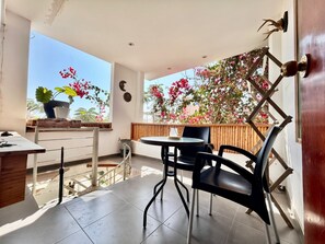 A balcony with a round table and chairs, potted plants, and a wooden bench.