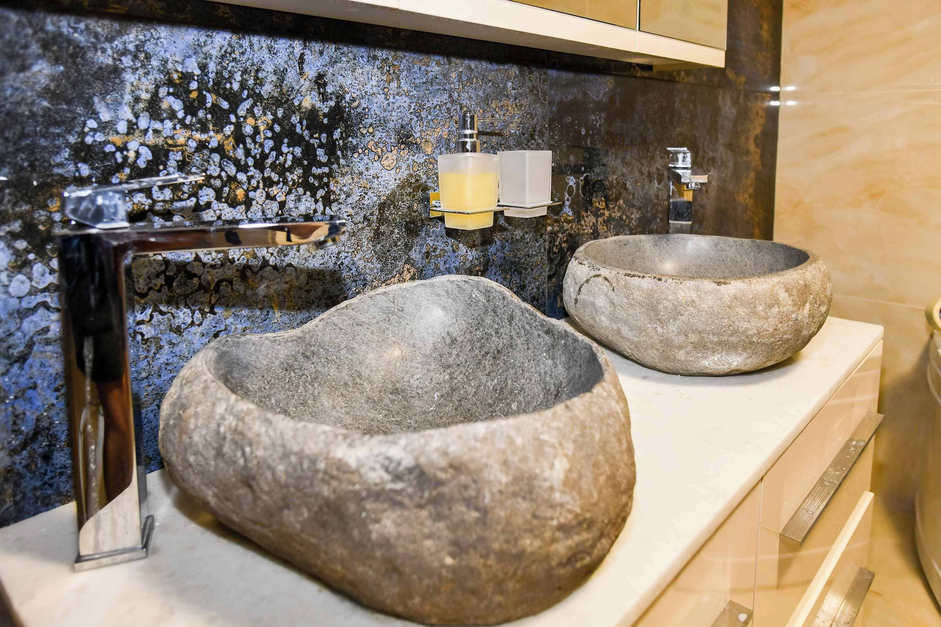 Un baño con dos lavamanos de piedra, un grifo moderno y una pared con textura.