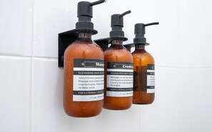 Three bottles of hair care products with pumps, labeled for cleansing and nourishing hair, mounted on a white tiled wall. - La Joya Azul SMA - LGBTQS (San Miguel de Allende)