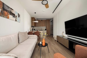 Un soggiorno moderno con un divano, un tavolino, una TV e una cucina sullo sfondo.