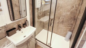 Un baño moderno con ducha de vidrio, lavamanos blanco y pared revestida de mármol.