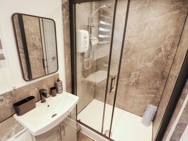 Un baño moderno con ducha de vidrio, lavamanos blanco y pared revestida de mármol.