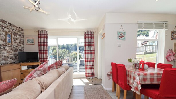 A cozy living room with a sofa, a TV, and a dining area with red chairs and a table. - Boos Bungalow (Gunnislake)