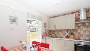 A kitchen with a red and white checkered tablecloth, white cabinets, a stainless steel oven, and a window with a view of the outside. - Boos Bungalow (Gunnislake)