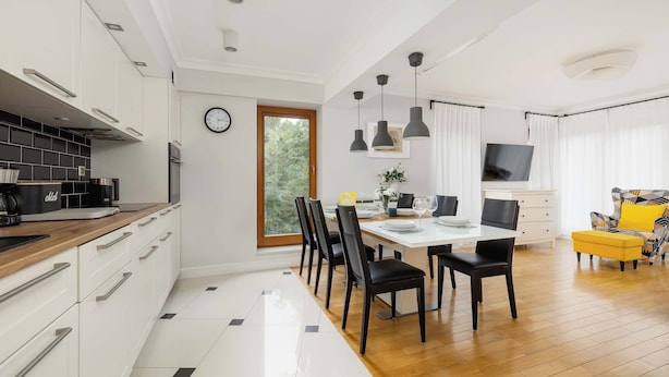 A modern kitchen with white cabinets, a wooden countertop, and a dining area with a table and chairs.