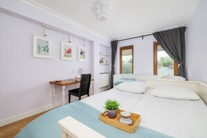 A bedroom with a bed, a desk, a chair, a window with curtains, and a tray with a plant and a cup.