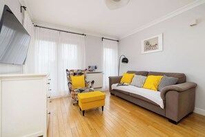 A living room with a sofa, ottoman, patterned armchair, and a flat-screen TV.