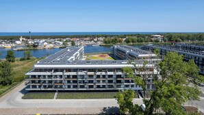 A modern building with multiple floors, a flat roof, and a sports field in the center. - Bright Apartment with Balcony | Spa Area and Parking (Dziwnów)
