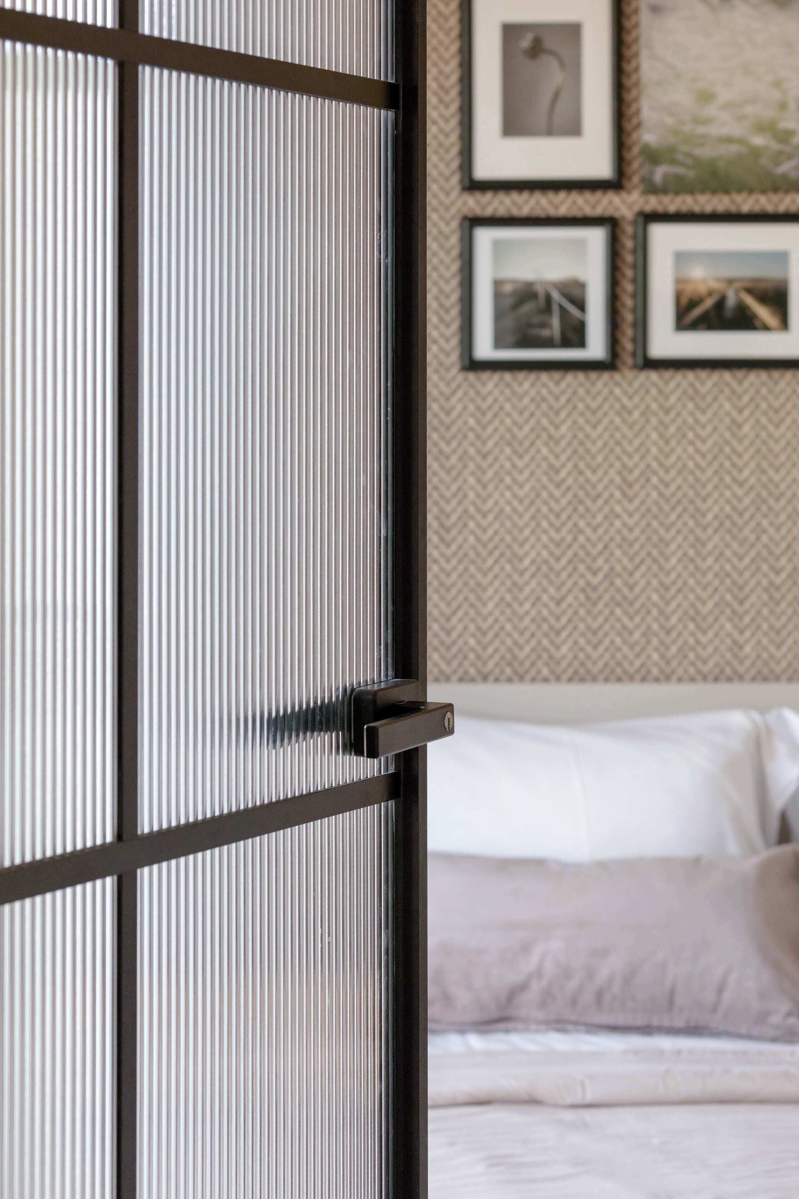 Une pièce avec un lit, un mur orné de tableaux encadrés et une porte coulissante à motifs verticaux.