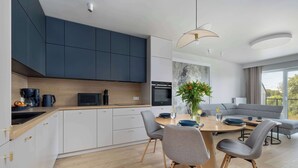 A modern kitchen with dark cabinets, a wooden countertop, and a dining area with a round table and chairs. - Bright Apartment with Balcony | Spa Area and Parking (Dziwnów)