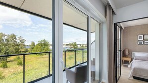 A bedroom with a large window, a balcony with a chair, and a view of greenery. - Bright Apartment with Balcony | Spa Area and Parking (Dziwnów)