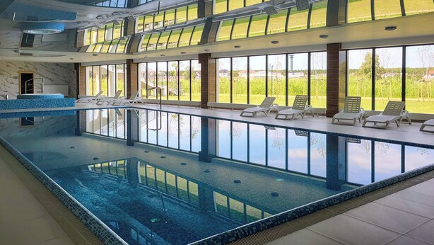 A large indoor swimming pool with clear views of the outdoors, sun loungers, and a modern architectural design. - Bright Apartment with Balcony | Spa Area and Parking (Dziwnów)