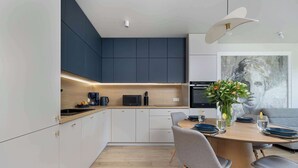 A modern kitchen with dark cabinets, a wooden countertop, and a dining area with a round table and grey chairs. - Bright Apartment with Balcony | Spa Area and Parking (Dziwnów)