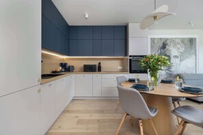 Uma cozinha moderna com armários escuros, bancada de madeira e área de refeições com mesa redonda e cadeiras cinzas.