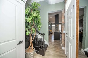A hallway with a staircase, a potted plant, and a kitchen area visible in the background.