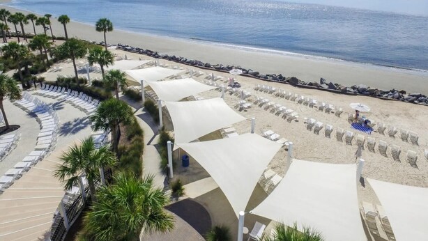 Een strandresort met rijen ligbedden en parasols, palmbomen en uitzicht op de oceaan.