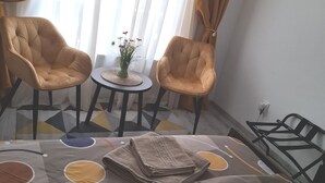 Et værelse med to lænestole, et lille rundt bord med en vase blomster og en seng med et mønstret sengetæppe.