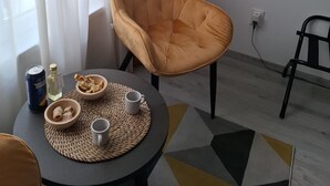 Et moderne værelse med et rundt bord, en polstret stol, en vævet bordskåner, en skål med snacks, en vandflaske og en sodavandsdåse.