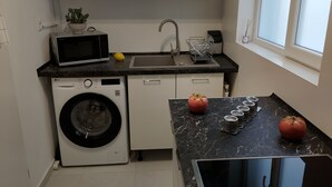 Et kompakt køkken med vaskemaskine, mikroovn, vask og et vindue.