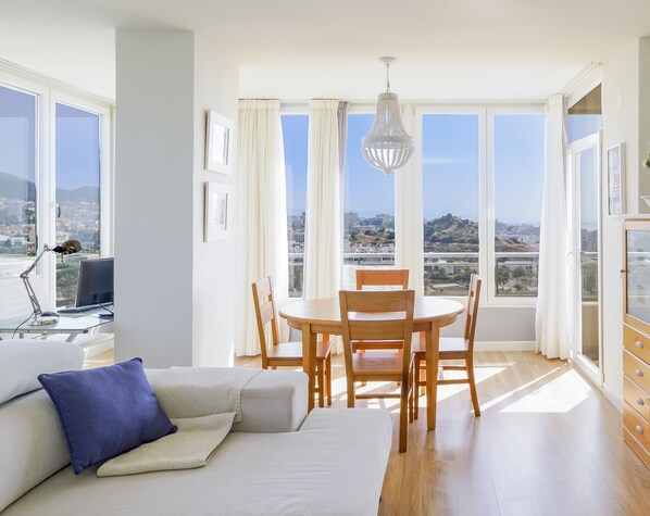 A modern living room with a dining area, large windows, and a city view.