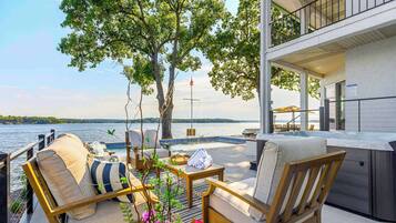 Une terrasse avec coin salon extérieur, un jacuzzi et vue sur un lac.