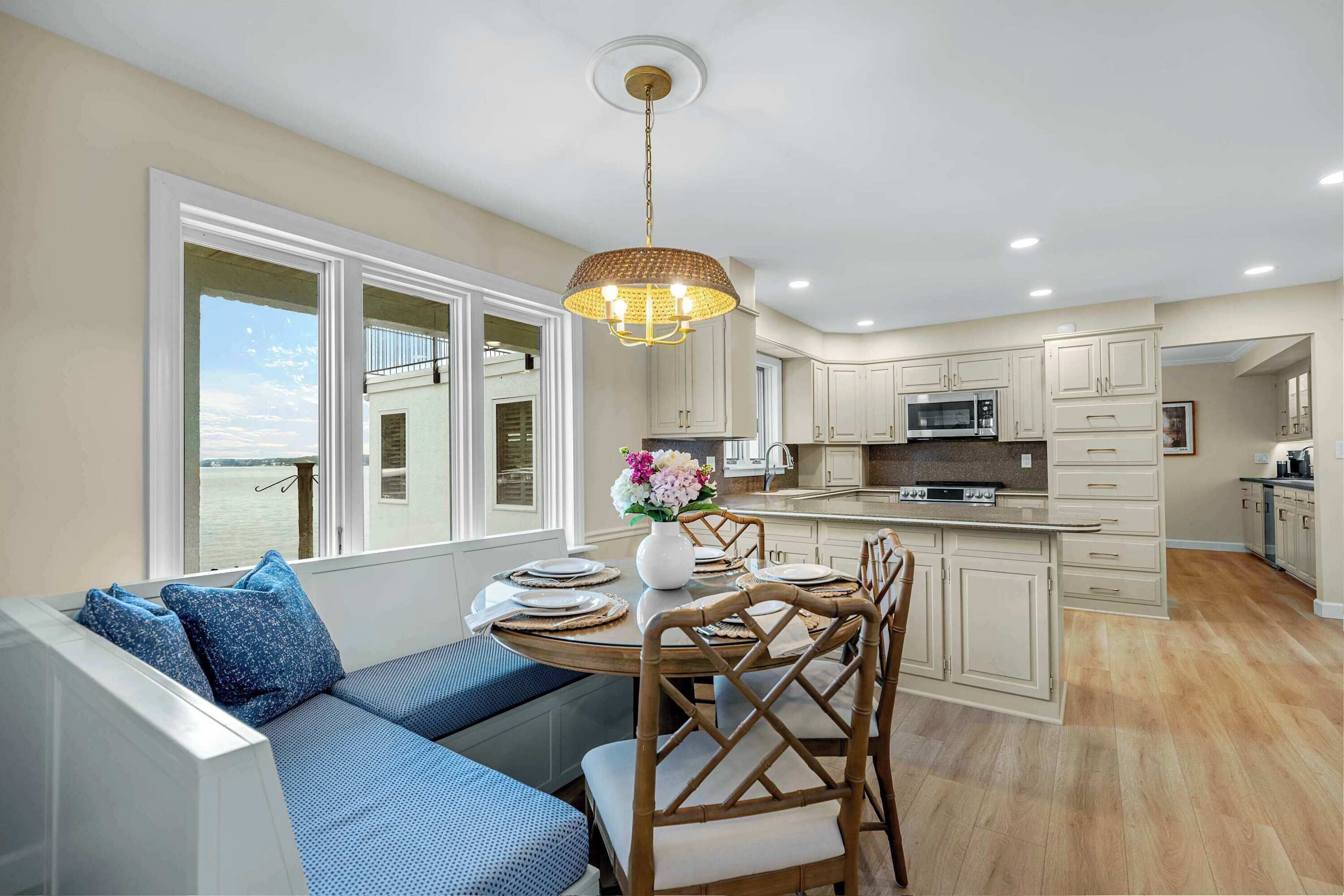 A modern kitchen with white cabinets, a central island, and a dining area with a view of the sea.