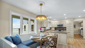 A modern kitchen with white cabinets, a central island, and a dining area with a view of the sea. - Panoramic Paradise – Lakefront Home for 15 w/ Game Room, Pool (Rocky Mount)