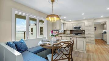 A modern kitchen with white cabinets, a central island, and a dining area with a view of the sea.