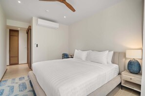 A modern bedroom with a large bed, a nightstand, a lamp, an air conditioning unit, and a ceiling fan. - Reef Residences, Three-Bedroom 3302 3B Deluxe (Choeng Thale)