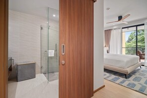 A modern hotel room with a glass shower, a wooden wardrobe, a bed with a view, and a ceiling fan.