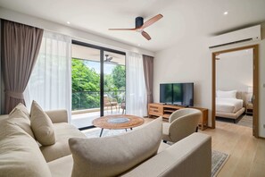 A modern living room with a sofa, TV, and a balcony with a view of greenery.