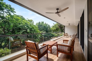 Un balcon doté de mobilier en bois, d’une rambarde en verre et offrant une vue sur une végétation luxuriante.
