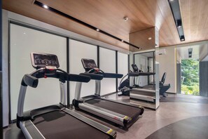 Une salle de sport moderne dotée de trois tapis de course, de grandes fenêtres et d’un plafond en bois.