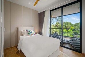 Une chambre dotée d’un grand lit, d’un ventilateur de plafond et offrant une vue sur une végétation luxuriante grâce à une porte-fenêtre coulissante.