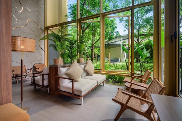 A modern interior with a sofa, chairs, and a table near large windows overlooking a garden.