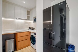 Cocina moderna con armarios blancos, lavadora y refrigerador de acero inoxidable.