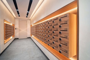 A hotel hallway with wooden lockers numbered 2101 to 2106, a door at the end, and a row of keys on the left wall.