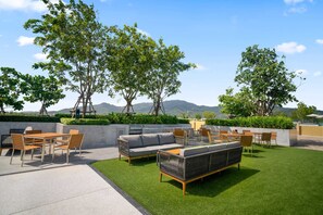 An outdoor patio with a dining set, sofa, and chairs, surrounded by greenery and trees, with a view of distant hills. - Reef Residences, Three-Bedroom 3505 3B Premium (Choeng Thale)