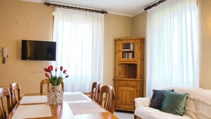 Un comedor con una mesa de madera, sillas, un florero con flores, un televisor en la pared y un mueble de madera.