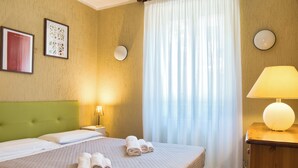 Habitación de hotel con una cama, dos lámparas adosadas a la pared, una mesita de noche y un aparador de madera.