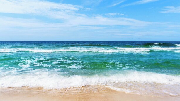 A beach with waves crashing onto the shore under a clear sky.