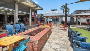 An outdoor seating area with colorful chairs and tables, a brick fire pit, and a view of the restaurant 'HOOKED' in the background.