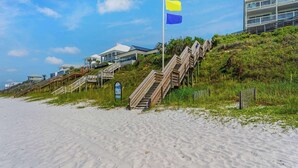 A beachside property with wooden staircases leading to a building, a flag, and a sandy beach.