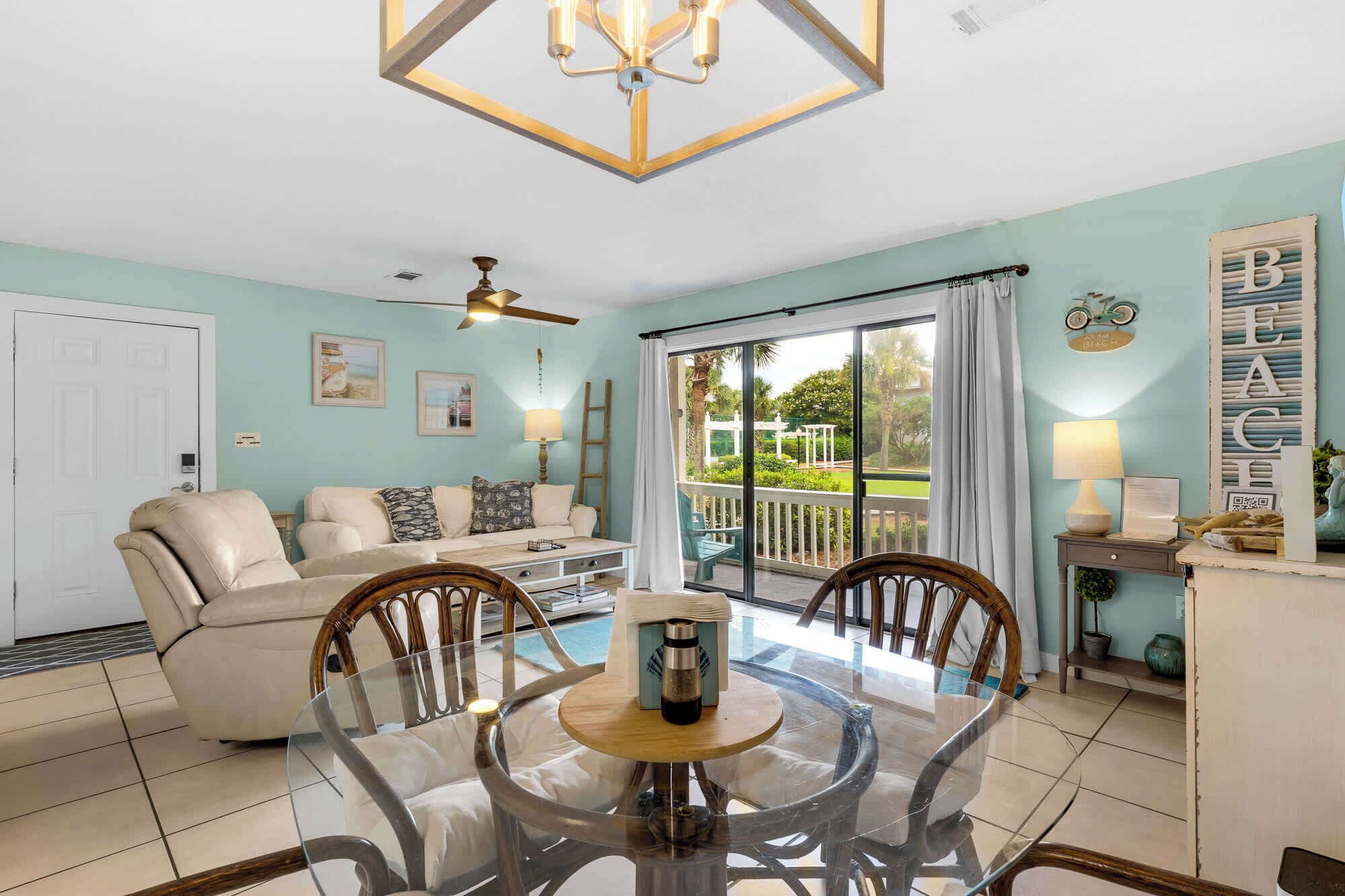 A spacious living room with a glass dining table, a sofa, and a ceiling fan.